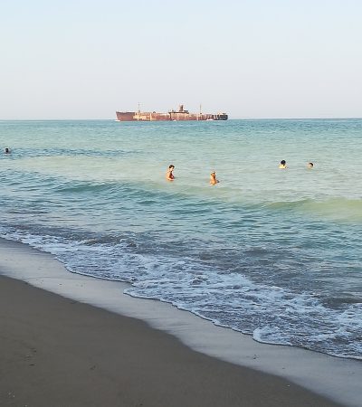 fasie de nisip cu mare in mai multe nuante de albastru, vapor in larg si oameni in apa