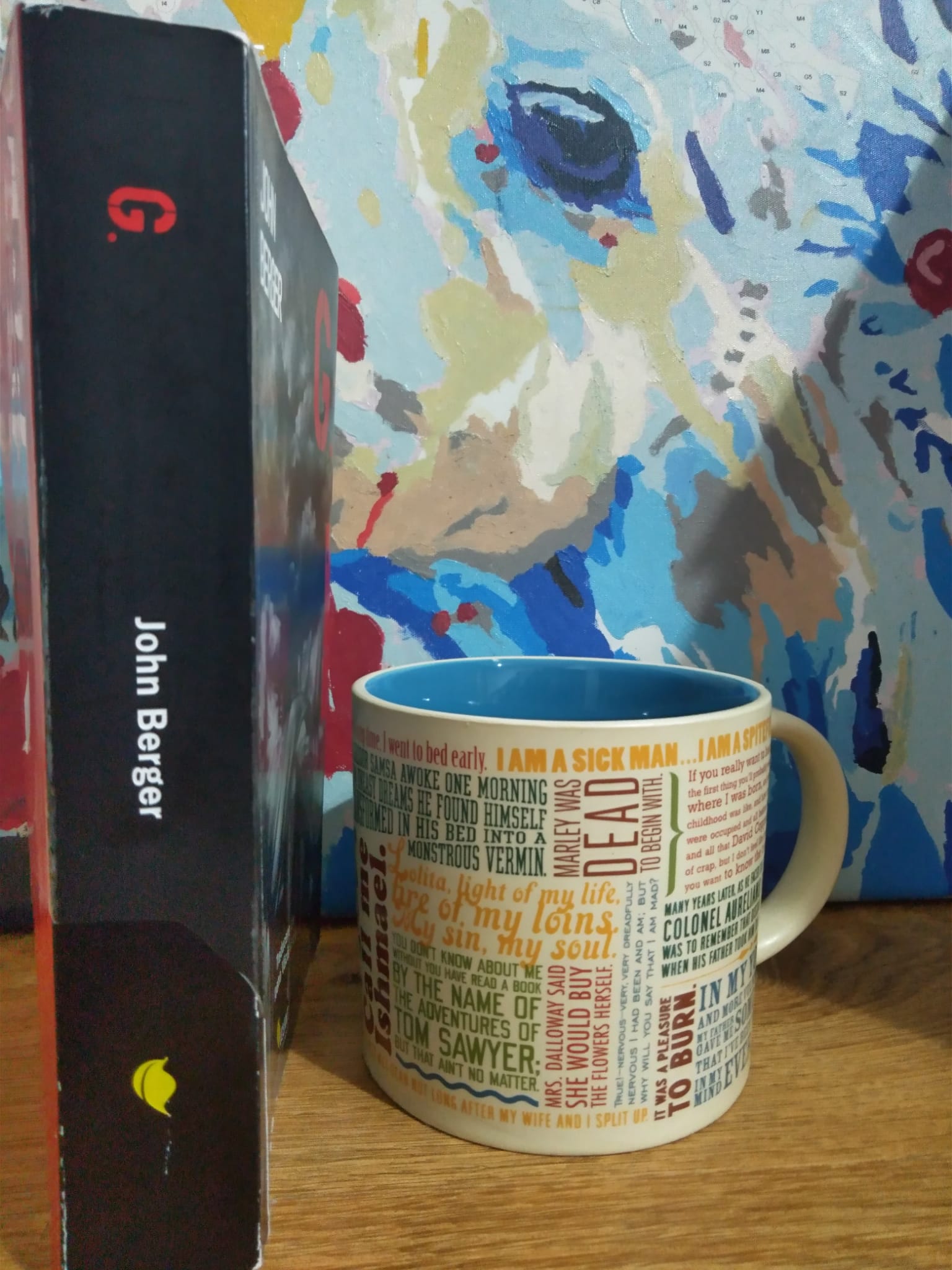 Poză cu coperta cărții "G." văzută din lateral, se pot citi titlul și autorul; în partea dreapta a imaginii se află o cană de cafea sau ceai.