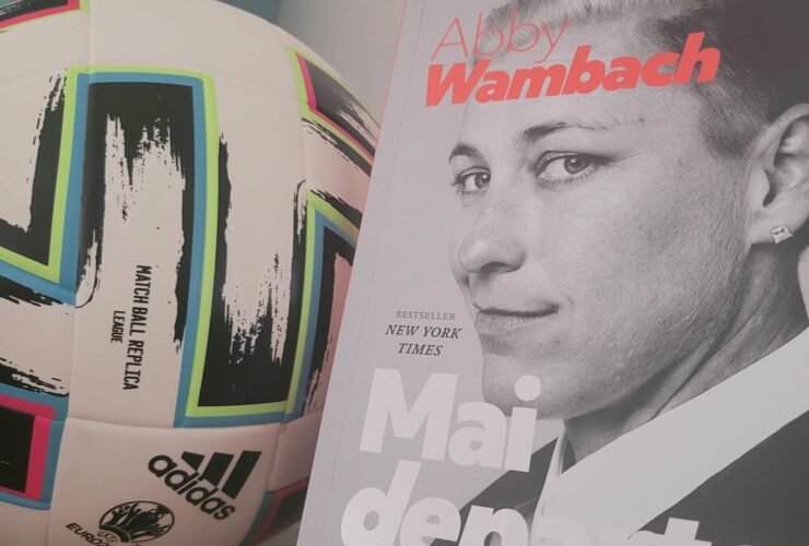 Cartea „Mai Departe” scrisă de Abby Wambach lângă mingea de fotbal de la Euro 2020.