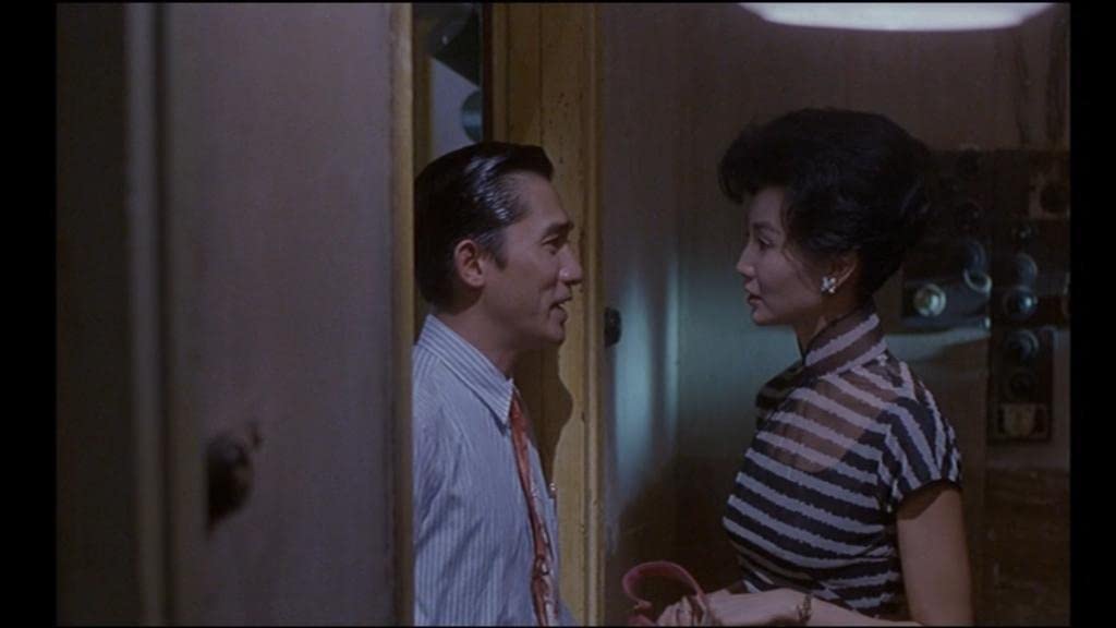Cele două personaje din filmul „In the Mood for Love” discutând în pragul ușii unui apartament.